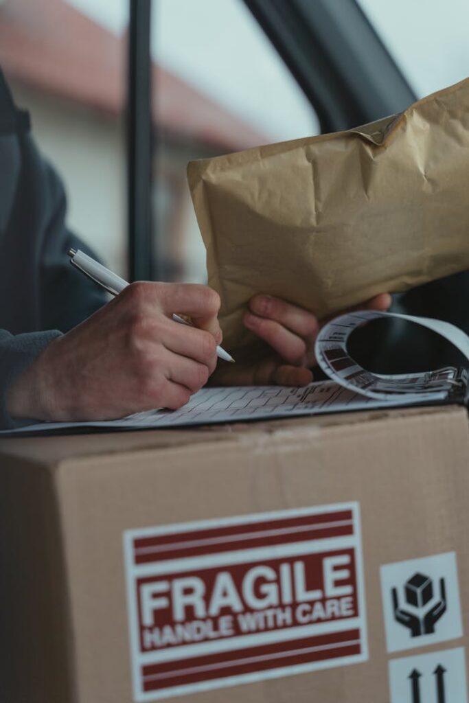 Close-up of a courier writing on a clipboard with a fragile package inside a vehicle.